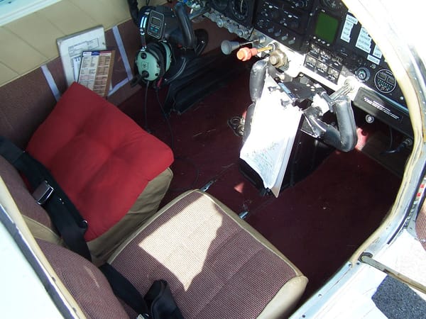 The cabin looking in from the right, showing the front seats, a headset and a kneeboard on the yoke